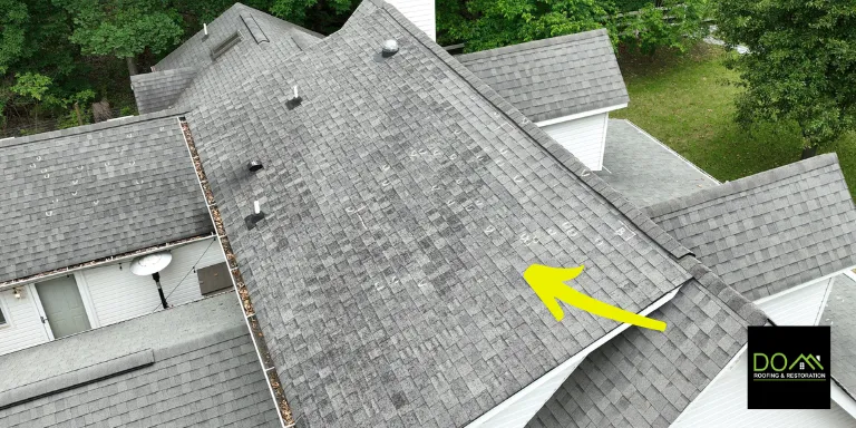 An aerial view of significant wind damage on a roof in Duluth, with arrows showing a lifted ridge cap and creased shingles needing repair by Dom Roofing & Restoration.