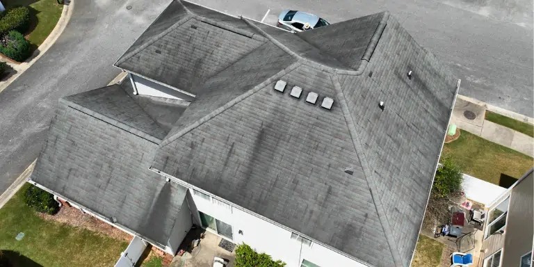 Roof Damage Caused by Moss | Roof Replacement Needed Close-up of thick moss on a roof lifting the shingles, a clear sign of moisture damage and a roof in critically bad condition.