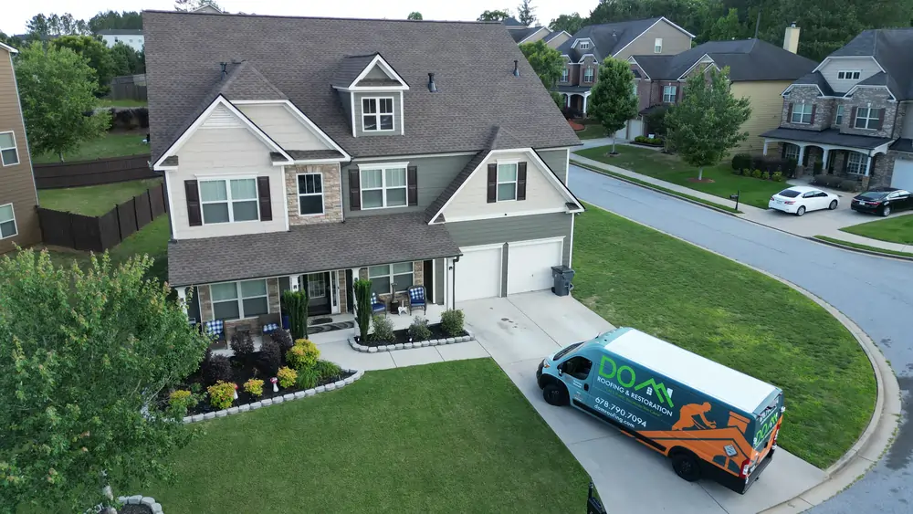 A beautiful suburban home with a new architectural shingle roof recently installed by DOM Roofing & Restoration, whose branded work van is parked in the driveway.