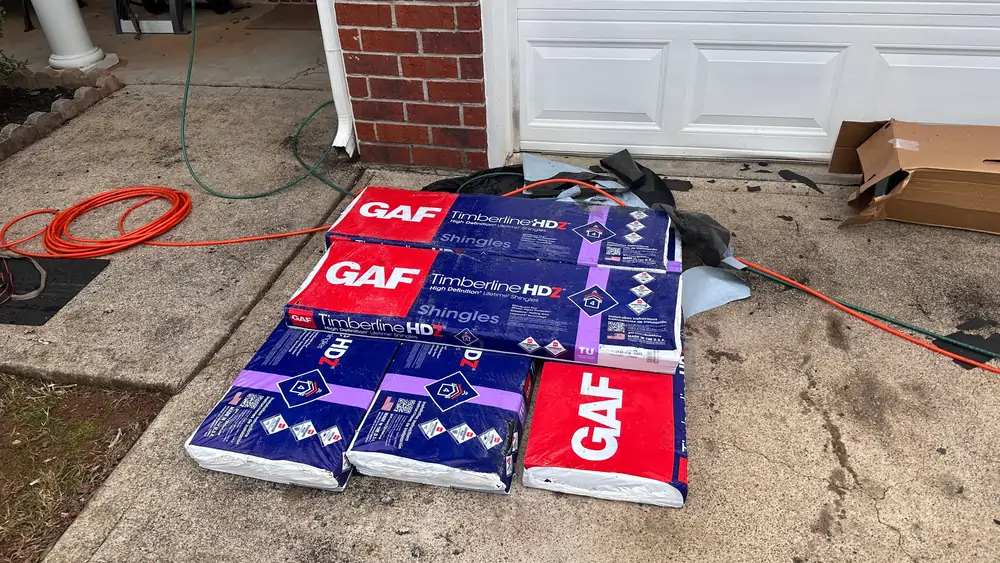 Bundles of GAF Timberline HDZ architectural shingles stacked on a driveway, ready for a new roof installation by the expert team at DOM Roofing & Restoration.