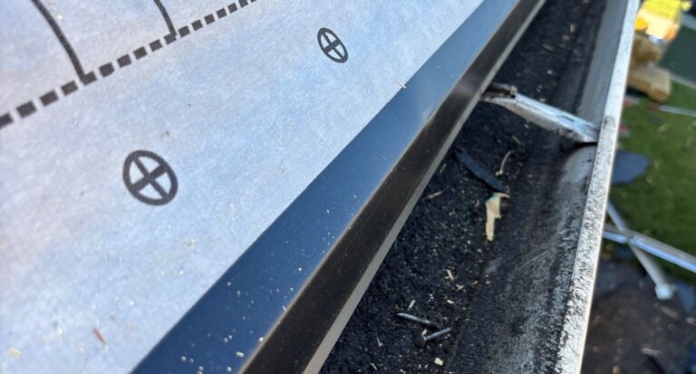 Metal drip edge along an eave beside a gutter and synthetic underlayment