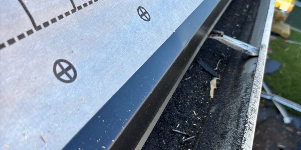 Metal drip edge along an eave beside a gutter and synthetic underlayment