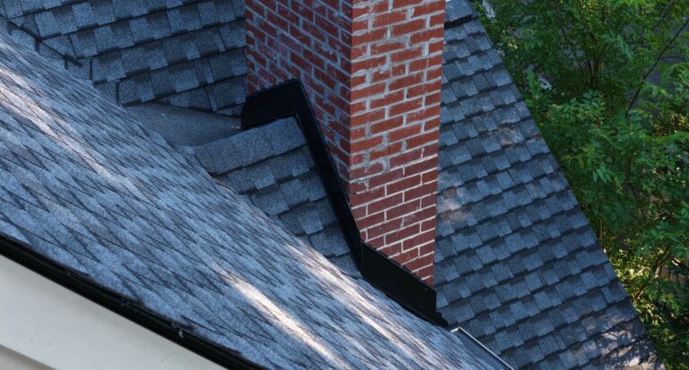 Metal flashing at the base of a brick chimney on a shingle roof