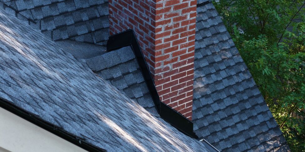 Metal flashing at the base of a brick chimney on a shingle roof