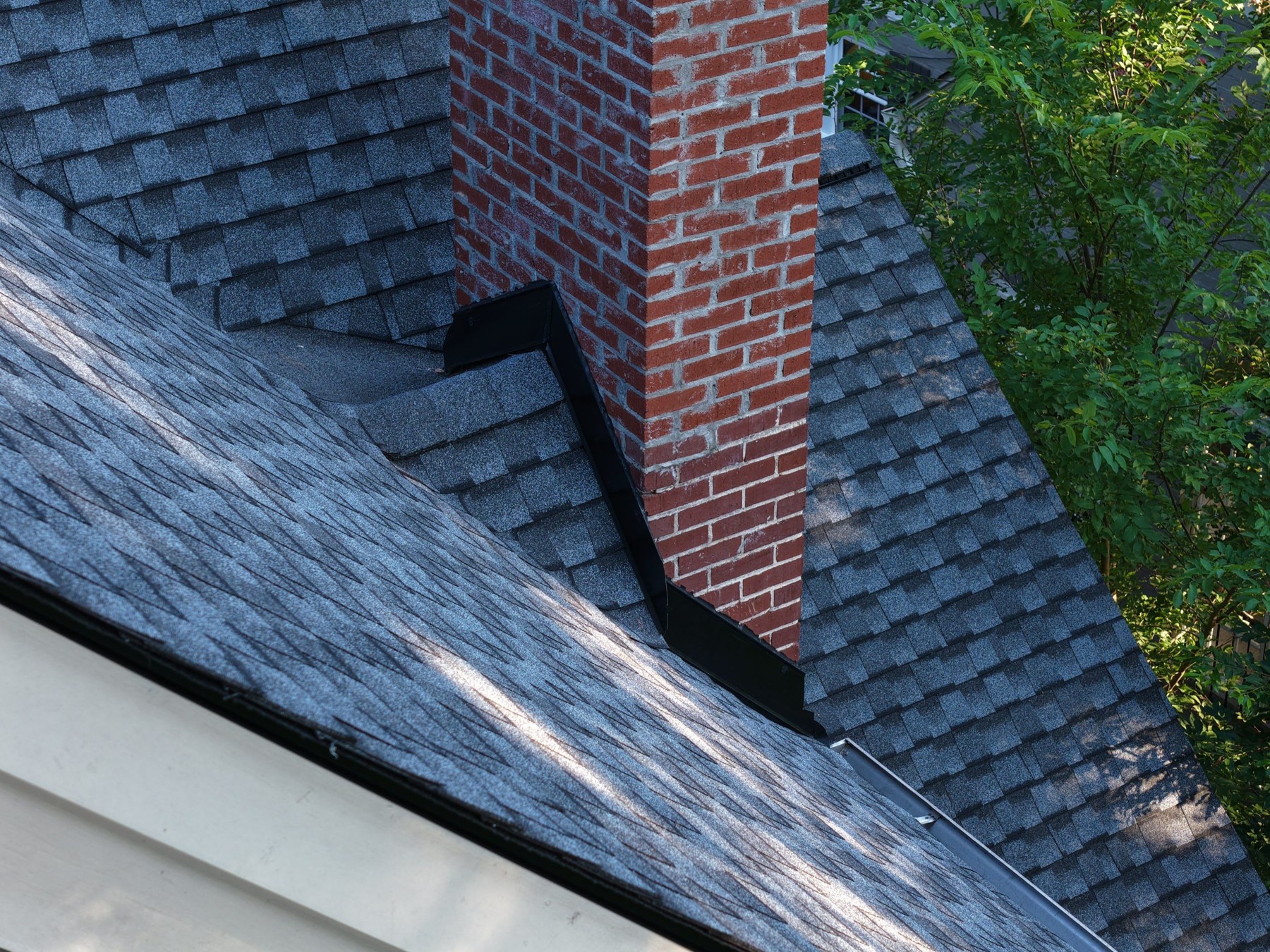 dom-real-flashing-01 Metal flashing at the base of a brick chimney on a shingle roof