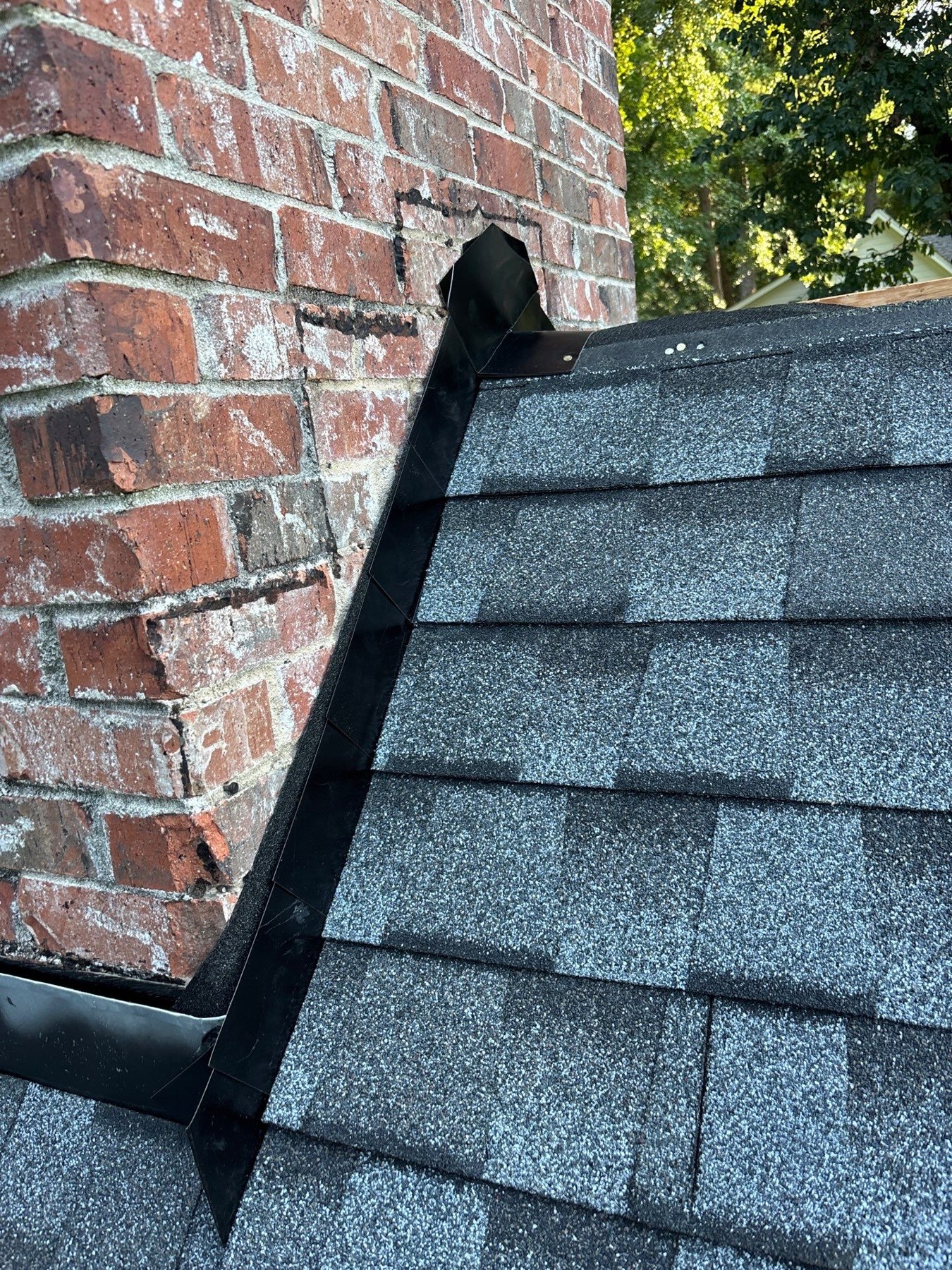Roof Flashing Guide: Types, Leaks & Repair Cost (2026) 1 Close-up of metal chimney flashing beside asphalt shingles