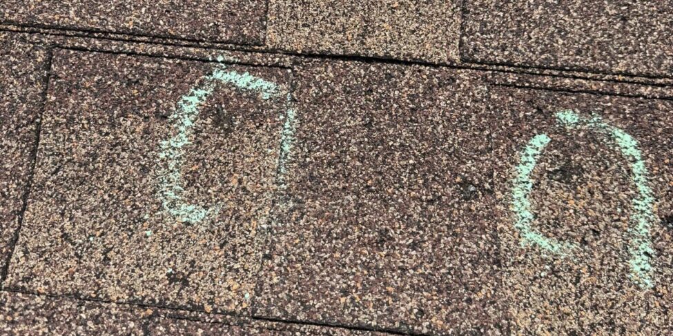Asphalt shingles with two impact areas circled in green chalk during a roof inspection