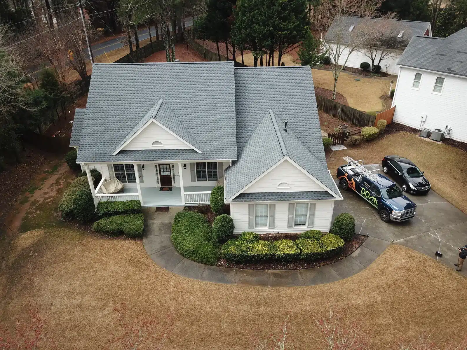 DOM Roofing and Restoration completed gable roof Light gray shingle roof over a white house with a front porch and garage, with a DOM Roofing and Restoration truck in the driveway.
