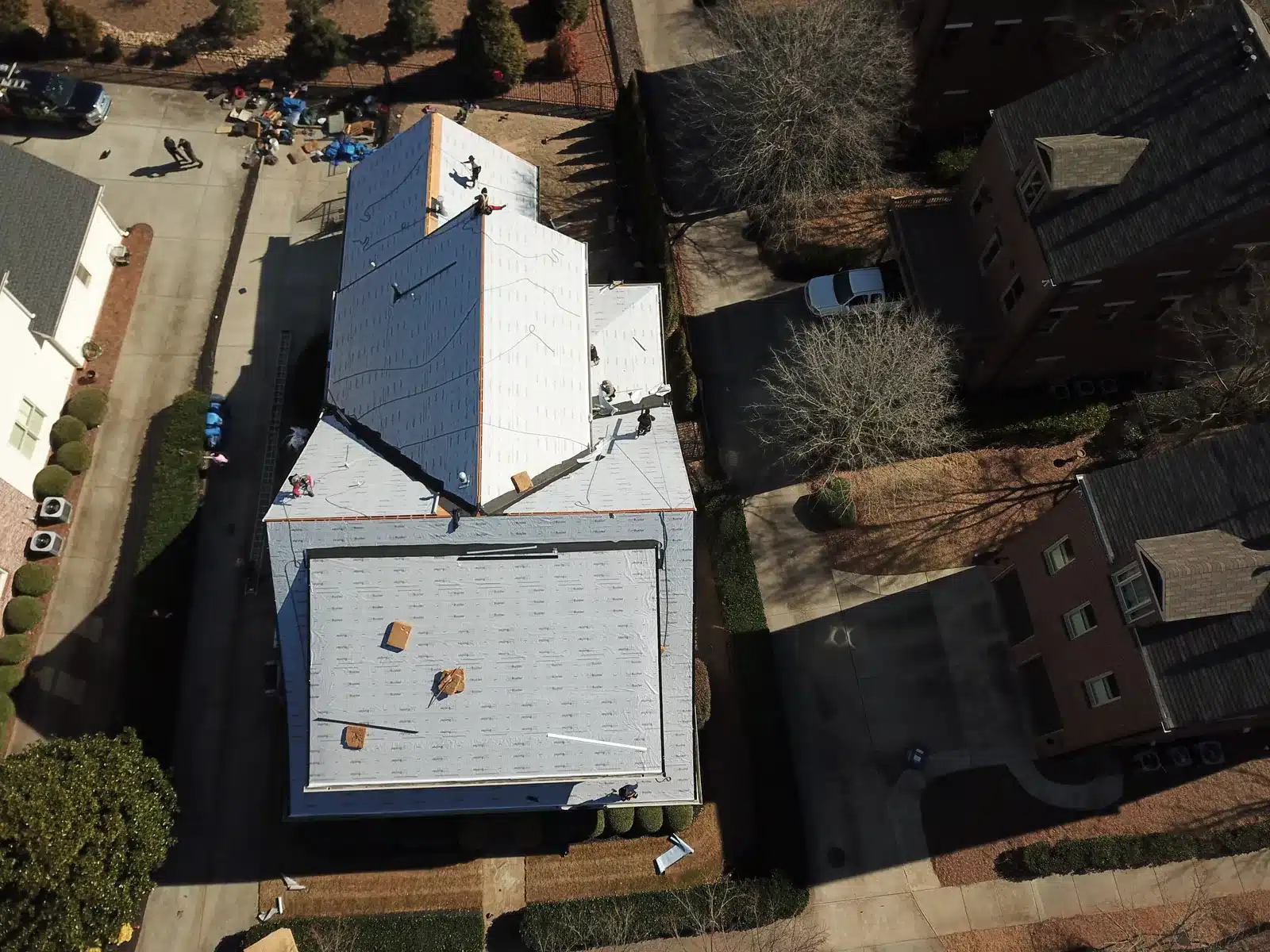 DOM Roofing and Restoration roof replacement in progress Overhead view of roofing crews working on a house covered with white roof underlayment before shingle installation.