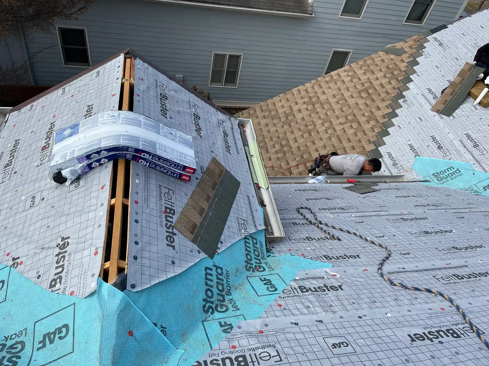 DOM Roofing and Restoration roofing layers during installation Roof replacement in progress with white underlayment, blue leak-barrier material, an open ridge slot and partially installed brown shingles.